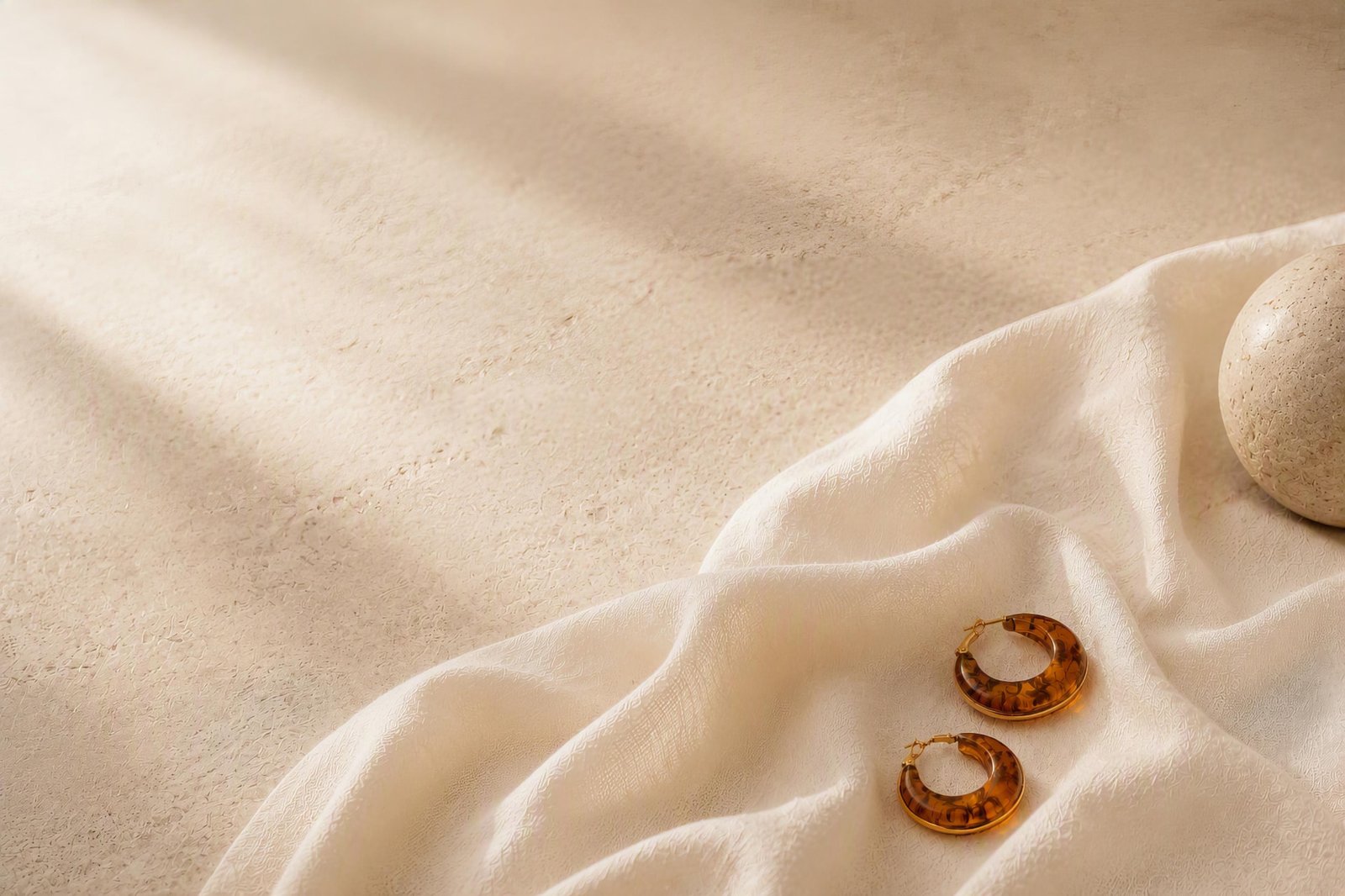 Amber acetate hoop earrings resting on ivory silk beside a smooth river stone