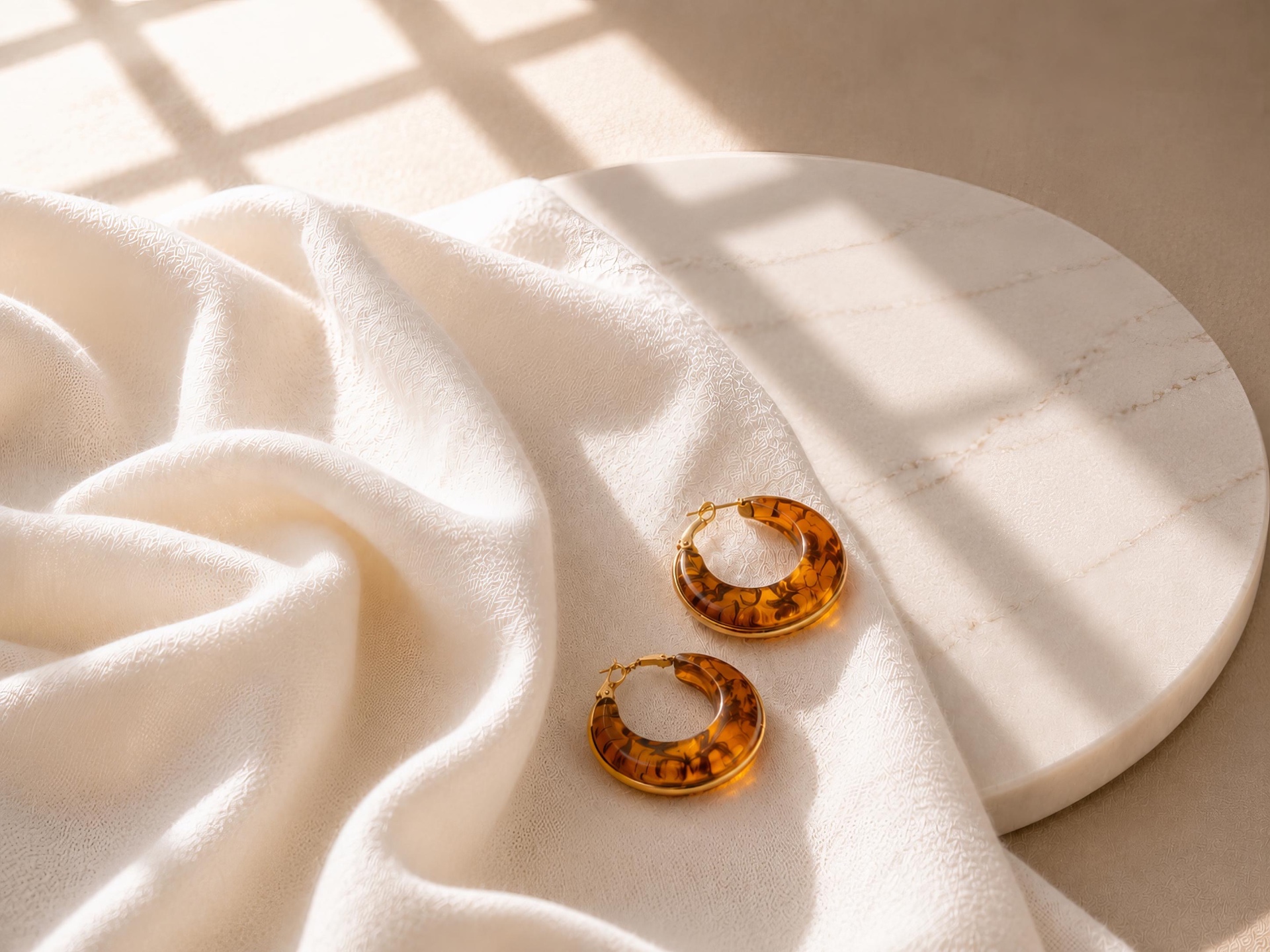 Amber acetate gold hoop earrings resting on a marble plate in soft window light